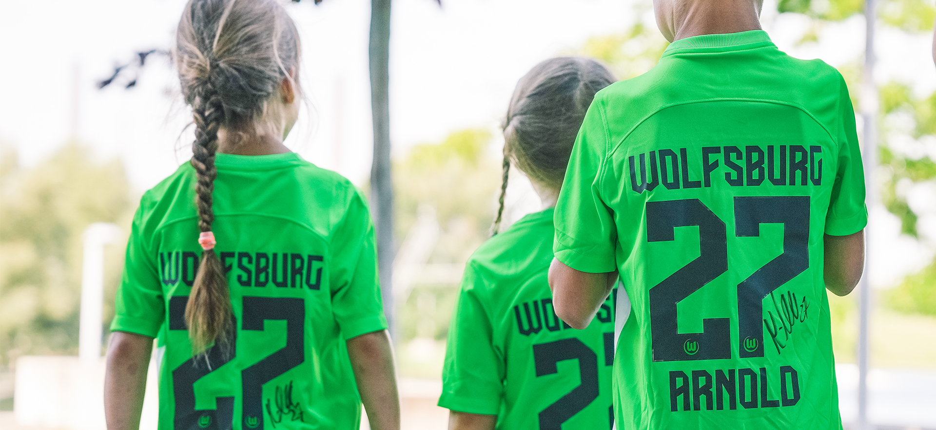 Drei kleine Kinder tragen signierte VfL Trikots.
