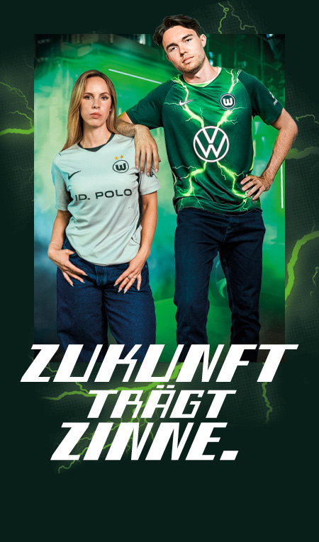 Zwei Personen tragen VfL-Wolfsburg-Trikots neben dem Schriftzug „ZUKUNFT TRÄGT ZINNE
