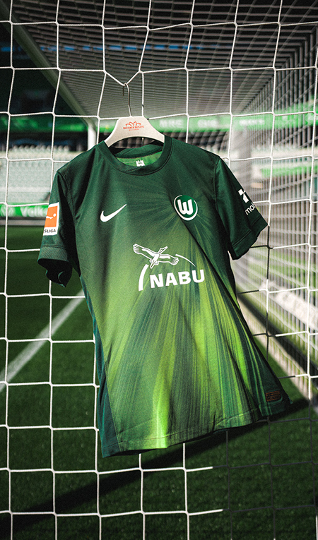 VfL-Wolfsburg-Trikot mit NABU-Schriftzug hängt in einem Tornetz im Stadion.