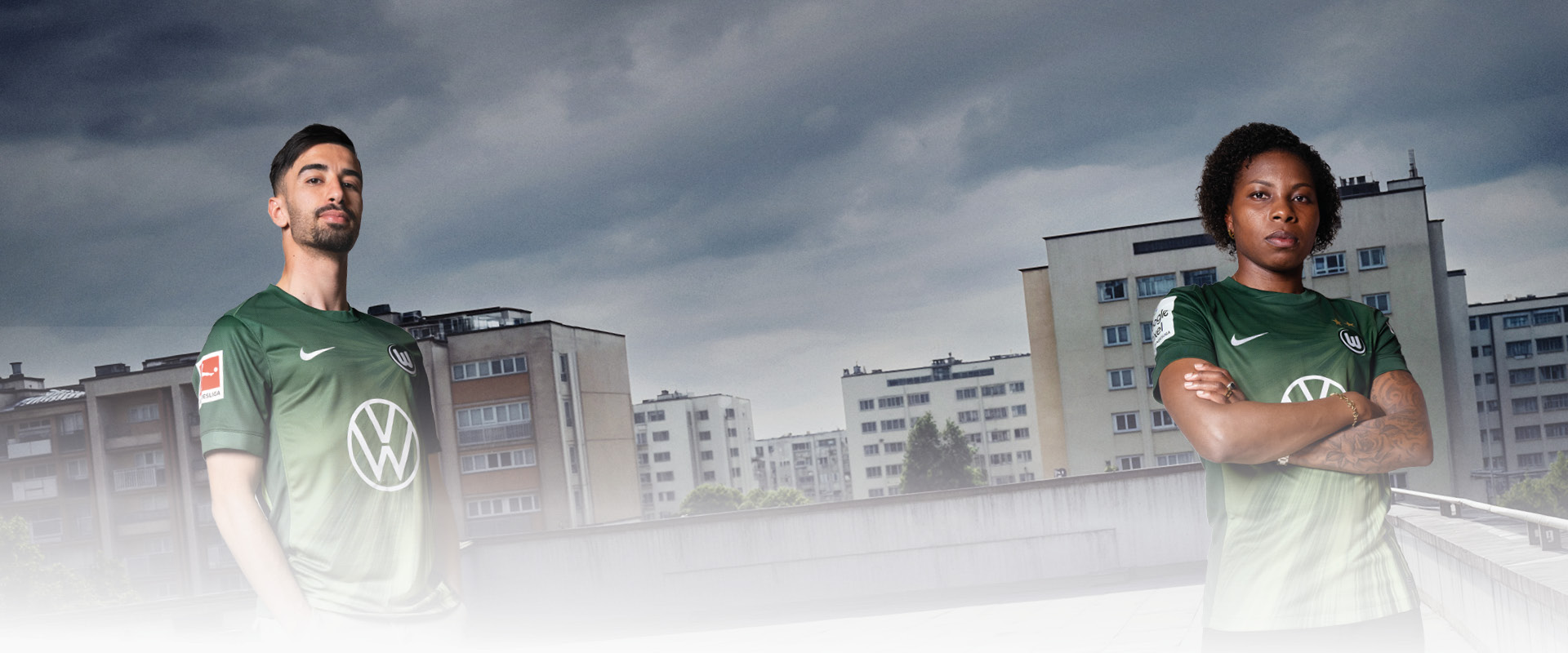 Hier wird das neue Heimtrikot präsentiert. Zwei Personen im grünen Heimtrikot stehen vor einer Stadt-Kulisse.