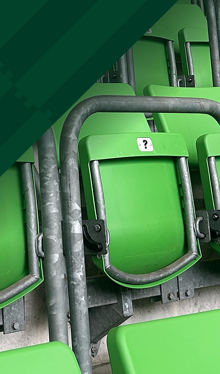 Grüne Stadionsitze mit Metallgeländern und einem schwarzen Fragezeichen auf einem Sitz.