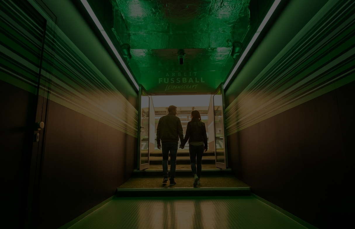 Ein Pärchen läuft Hand in Hand durch den Spielertunnel des VfL Wolfsburg auf das Spielfeld.