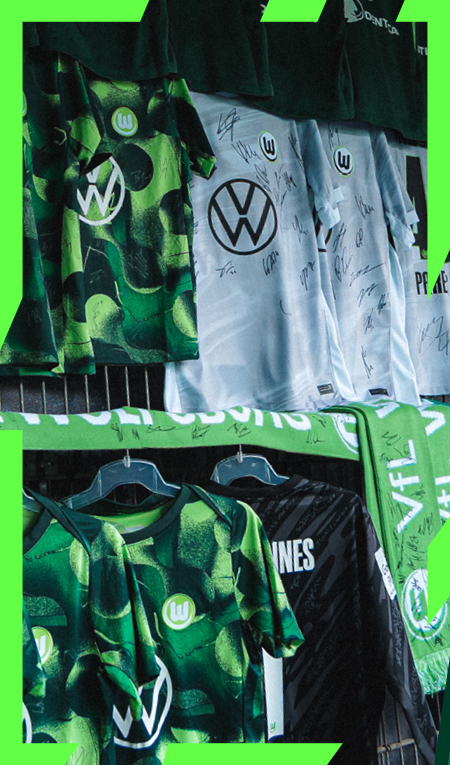 Signierte VfL-Wolfsburg-Trikots und Schals hängen an einem Verkaufsstand.