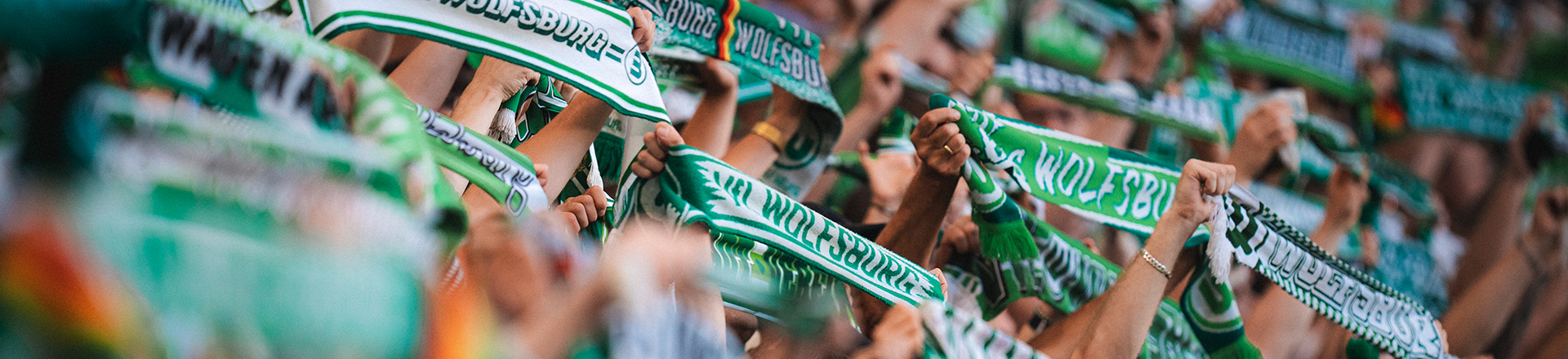 VfL-Wolfsburg-Fans halten grün-weiße VfL-Wolfsburg-Schals hoch.