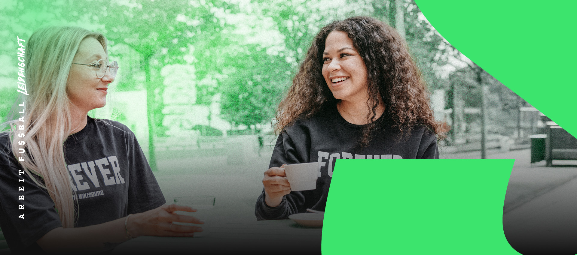 Zwei Frauen mit VfL Wolfsburg „Forever“ Fan-Shirts beim Kaffee im Freien.
