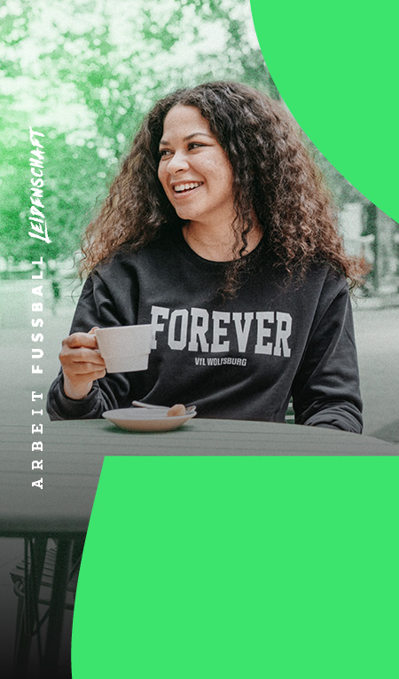 Frau mit schwarzem VfL Wolfsburg „Forever“ Sweatshirt beim Kaffee im Freien.