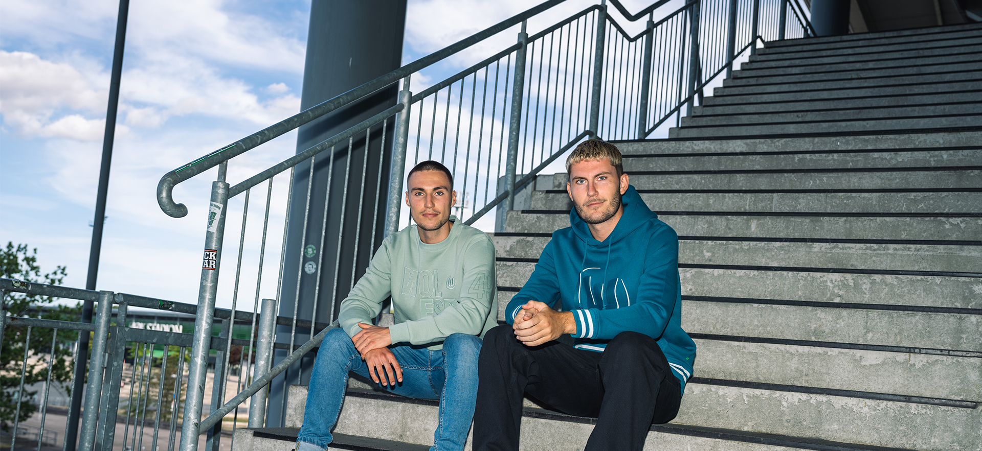 Zwei Spieler sitzen auf der Treppe und tragen VfL-Hoodies.