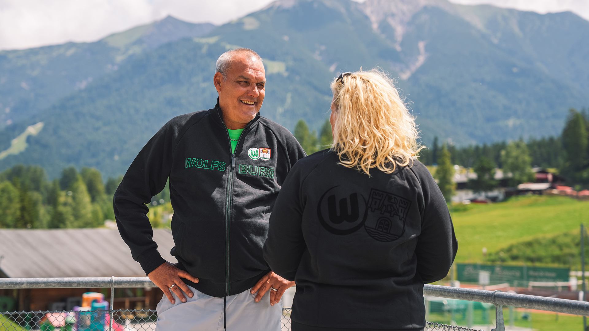 Balli unterhält sich mit einer Frau und trägt die Kultjacke des vfL Wolfsburg.